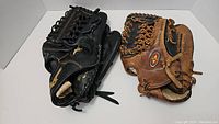 Two baseball gloves, one Easton brown leather glove and one Mizuno black leather glove, stacked together showing overall condition.