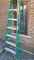 7 foot fiberglass step ladder, green frame with aluminum steps leaning against a brick wall beneath a window.