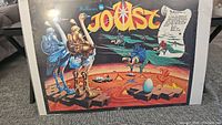 Full view of the Joust poster showing the game title, knights on large birds, and fantasy lava landscape.
