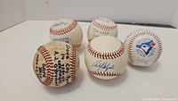 Five signed baseballs displayed on white surface, various autographs visible including a Toronto Blue Jays logo baseball