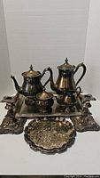 Full view of vintage silver plate tea set with teapot, coffee pot, sugar bowl, creamer, large serving tray, small decorative tray, and two ornate candle holders.