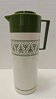 Front view of vintage Aladdin Beverage Butler thermos in green and cream with patterned decoration on body.