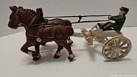 Full side view of the cast iron horse and buggy with driver, showing brown horse and white buggy with green driver.
