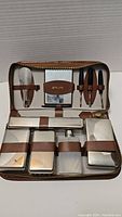 Open vintage brown leather zippered grooming case showing neatly arranged grooming tools and containers held with brown leather straps inside.