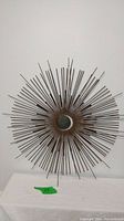 Full view of metal sunburst wall art showing circular central disc and radiating metal rods.