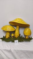 Front view of mustard yellow mushroom wall decor on green grass base