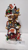 Front view of the Santa's Workshop music tower figurine showing the full height and details of elves, Santa, snow, and Christmas decorations.