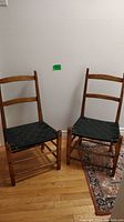 Pair of Shaker-style wooden chairs with black woven seats, positioned side by side showing overall condition and design.