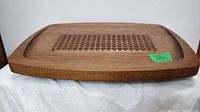 Top-down photo of rectangular teak carving tray showing grooved and textured raised triangle area in center and smooth border edges, with green lot number sticker.