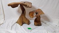Two handmade wooden mushroom sculptures, large and small, on white cloth