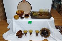 Lot of amber glass, brown Pyrex casserole, ceramic pieces arranged on white cloth