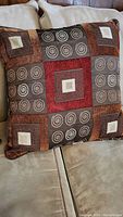 Photo of a square decorative pillow with geometric patchwork patterns in earthy tones on a beige couch.