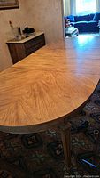 Close-up of the oval light brown wooden dining table showing wood grain pattern and rounded edges.