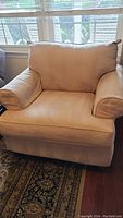 Front view of the light golden beige microfiber armchair showing plush armrests and seat cushion in a living room setting near a window.