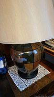 Close-up of lamp base showing ceramic patchwork design in shades of brown and green, with beige lampshade.
