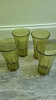 Four yellow translucent plastic glasses arranged on a wood floor, showing the front and side profile of glasses.