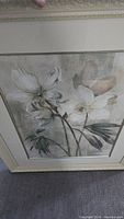 Full view of botanical art print of white flowers with green leaves, framed in cream ornate frame.