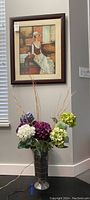 Full view with framed art hanging and mirrored vase with flowers arranged beneath it.