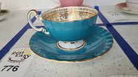 Side view of the Aynsley teacup and saucer showing the teal exterior and gold trim.