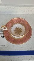 Teacup and saucer set shown side by side displaying pink and gold floral pattern with gold rims, photo taken to show design and condition.