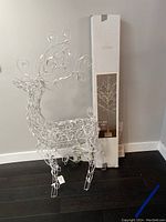White wire frame reindeer decoration standing on dark flooring, showing full body shape and decorative scrollwork with tall antlers.