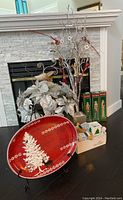 Wide angle shot showing several Christmas decorations including red tray, poinsettias, branch tree, and boxed ornaments