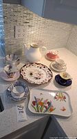 Wide view of all fine china items including teapot, plates, teacups with saucers, and platter arranged on countertop.