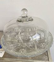 Clear crystal food cover with rounded top knob, sitting on plate under a white background.