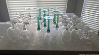 Top view of 18 pieces of glass and crystal stemware arranged on countertop with blinds in background.