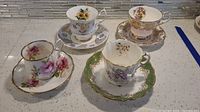 Four distinct teacup and saucer sets arranged on a countertop showing floral patterns and gold trim