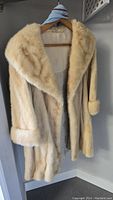 Full front view of the light beige mink fur coat hanging on a wooden hanger.