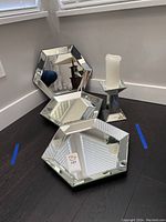 Photo showing three hexagonal mirrored trays stacked or arranged on a dark floor with a mirrored candle holder holding a white candle