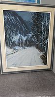 Full view of the framed original winter landscape painting showing snow-covered road, mountains and bare trees