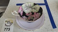 Teacup nestled in saucer showing floral interior and gold trim alongside lot number card