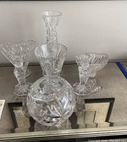 Photo showing multiple clear crystal vases and bowl with various shapes featuring pinwheel cut pattern.