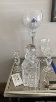 Crystal decanter with stopper, two crystal candle holders, and four stemmed glasses arranged on mirrored surface