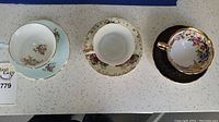 Three vintage teacups and matching saucers arranged in a row on a speckled countertop, showcasing their floral patterns and gold accents.