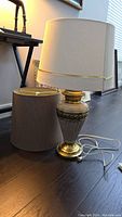 Table lamp displayed with beige fabric shade installed and a second darker brown fabric shade resting beside it.