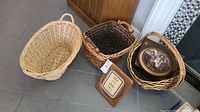 Three woven wicker baskets, two smaller baskets and one light natural large basket, with two framed vintage photos and one wooden plaque visible.