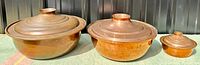 Photo showing full set of three antique copper covered serving dishes arranged from largest to smallest with lids on.