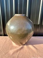 Front view of a large rounded pottery vase with dark redware finish outdoors on fabric surface