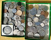 Two green boxes filled with assorted old coins of various sizes and metals, some silver coins are visible, with one coin encased in plastic in one box.