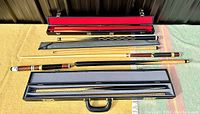 Overview of three pool cues laid out with two open hard cases