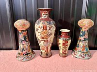 Front view showing pair of Satsuma porcelain candlesticks and two vases, arranged lined up on a surface with dark background.