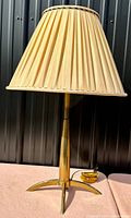 Full view of lamp with pleated fabric shade and polished brass base with tripod feet.