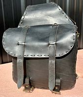Front view of one black leather saddle bag showing flap closure with two buckle straps and leather lace edging.
