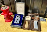 Overview photo of all lighters including fire hydrant lighter, Builtton lighter in box, Win butane lighters in boxes, Bentley lighter, and small case.
