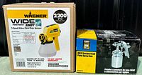 Two boxes side by side showing the Wagner Wide Shot Power Painter Plus and the Power Fist HVLP suction feed paint spray gun.