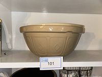 Front side view of one light brown ceramic mixing bowl with embossed patterns on shelf