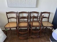 Six wood framed dining chairs with cane woven seats arranged in two rows against a wall.